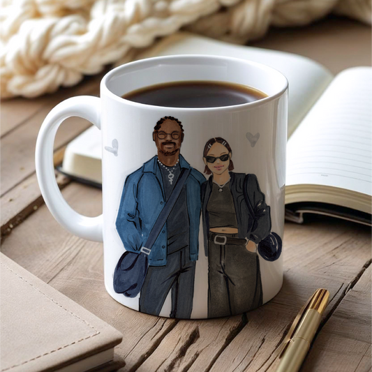 Mug with a design of two people on a wooden surface with a blanket and notebook.