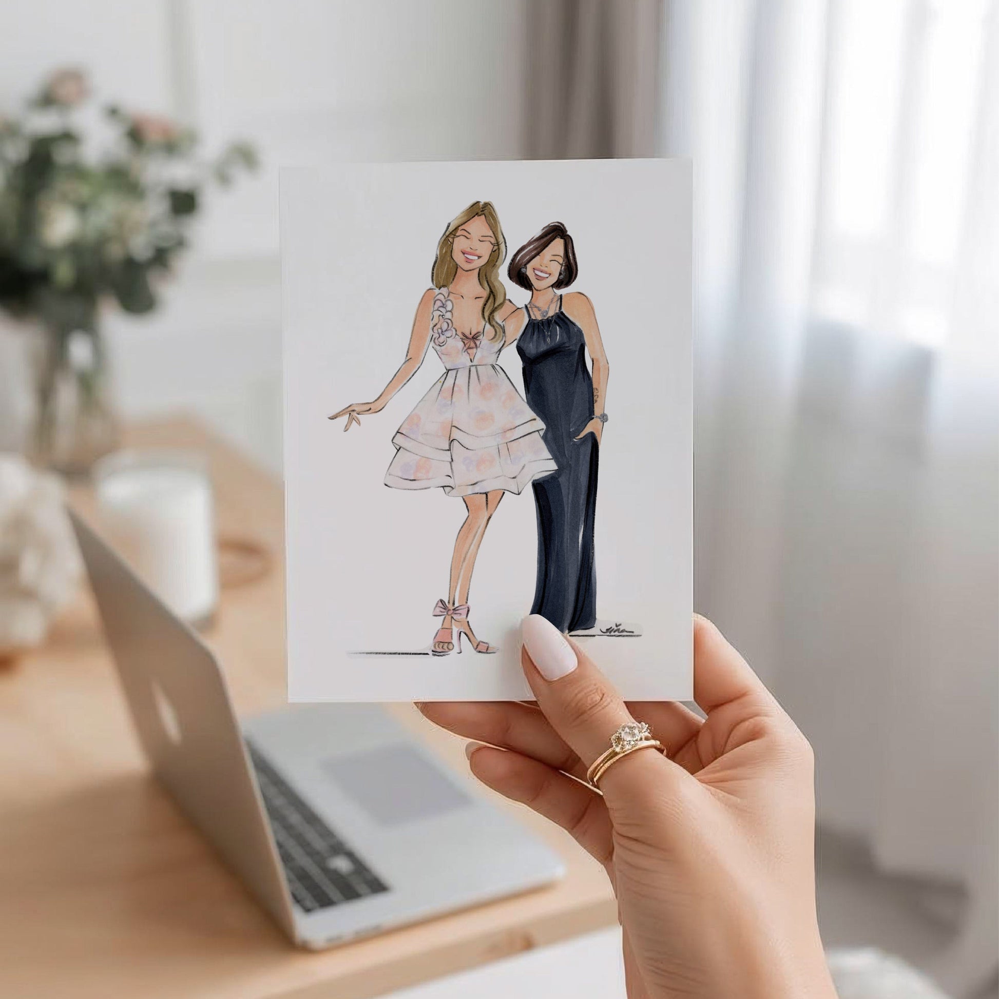 Women's hand holding a card with a fashion illustration of two woman.