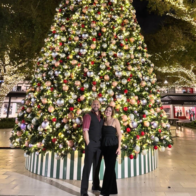 Two people standing in front of a large decorated Christmas tree at night.