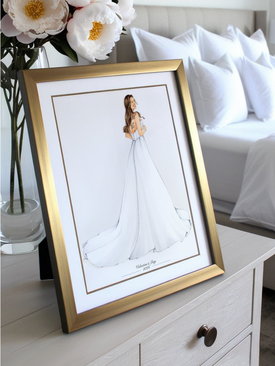 Framed illustration of a bride by Keepsake Couture, displayed on a dresser with flowers and pillows in the background